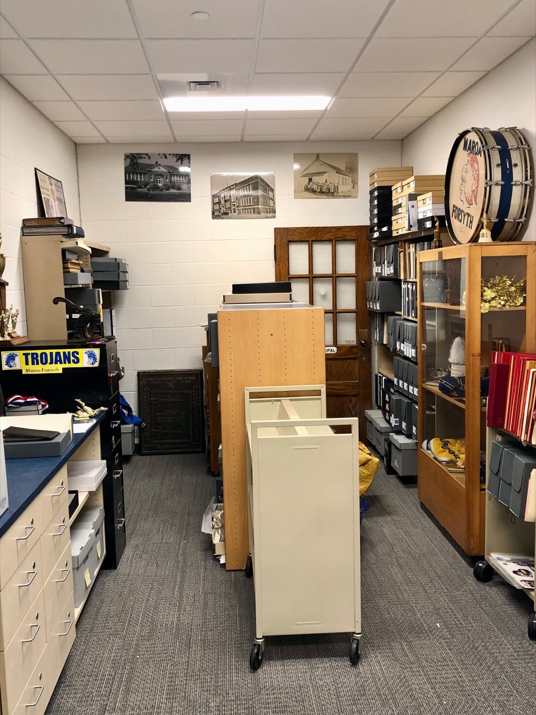 Shelves, document boxes, photographs, and school artifacts inside the archive room