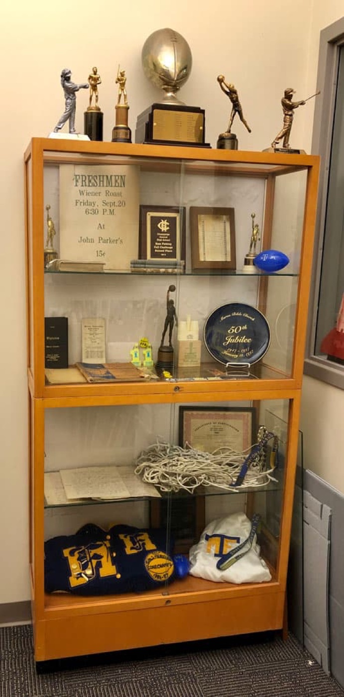 Archive display case containing trophies, awards, school clothing, and memorabilia
